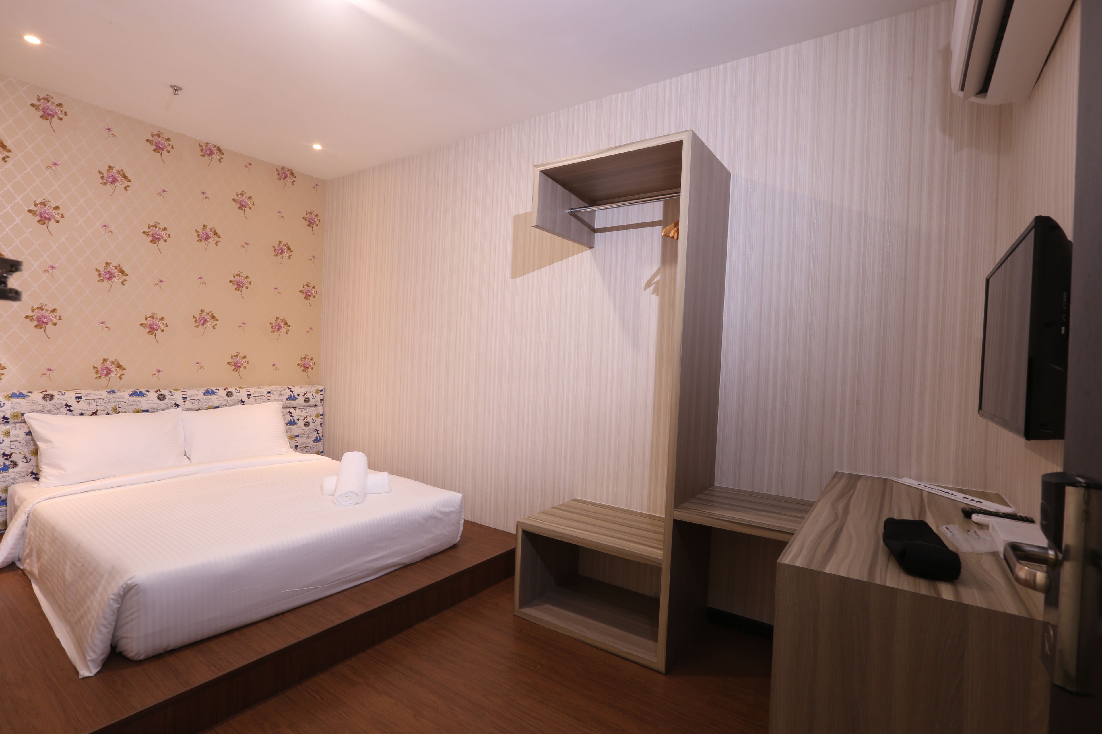 A modern hotel room with a bed, a wooden desk, and a built-in wardrobe.