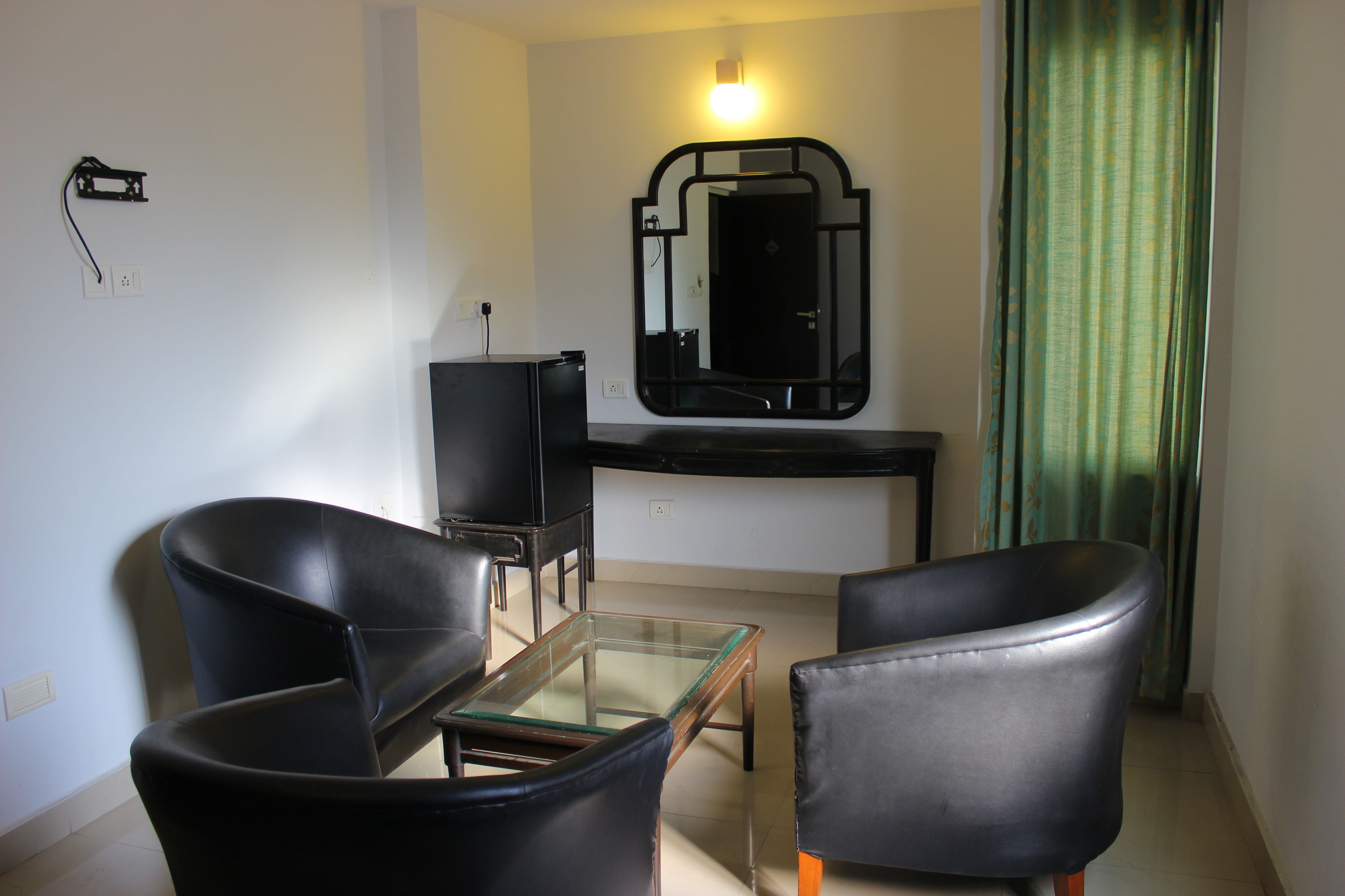 Una pequeña sala de estar con dos sillones de cuero negro, una mesa de centro de vidrio, un mueble de entretenimiento negro y un espejo con marco negro.