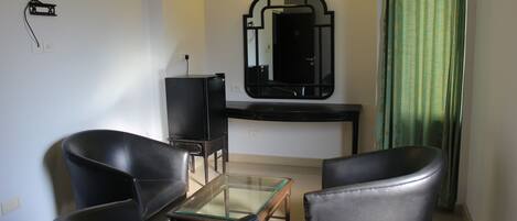 Una pequeña sala de estar con dos sillones de cuero negro, una mesa de centro de vidrio, un mueble de entretenimiento negro y un espejo con marco negro.