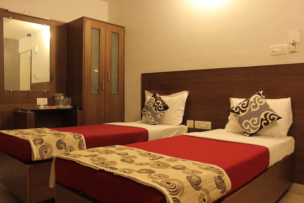A hotel room with two beds, each with a red bedspread and a patterned throw. There is a wooden wardrobe and a mirror on the wall.