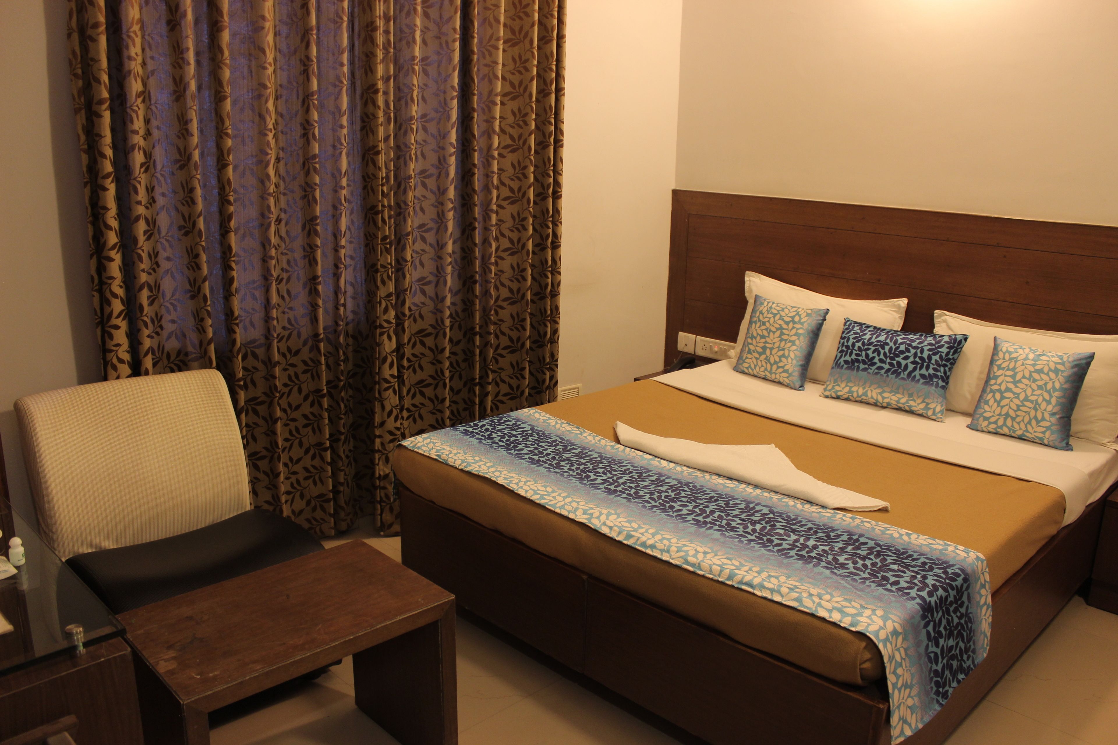 A hotel room with a large bed, a wooden headboard, and a patterned curtain.
