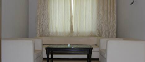 Una sala de estar con un conjunto de sofá, una mesa de centro y un ventanal con cortinas.