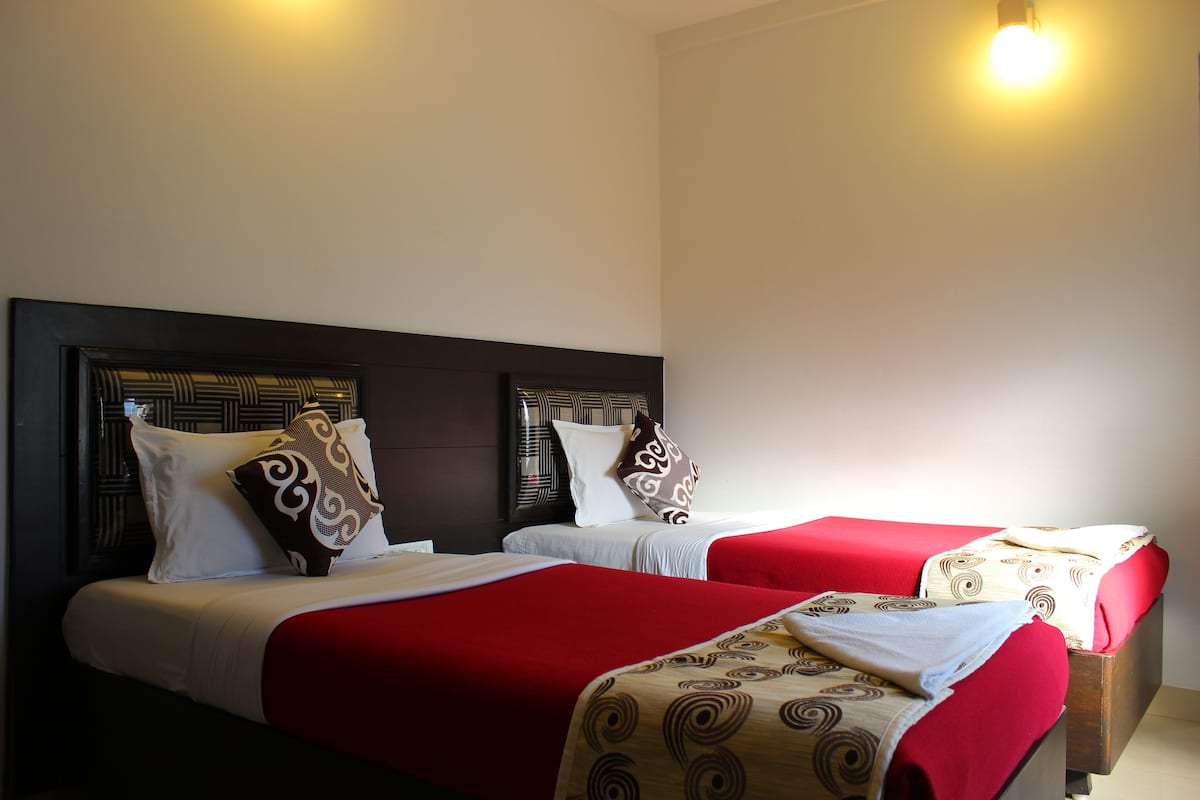 A hotel room with two beds, each with a headboard, white bedding, and red and patterned bedspreads.