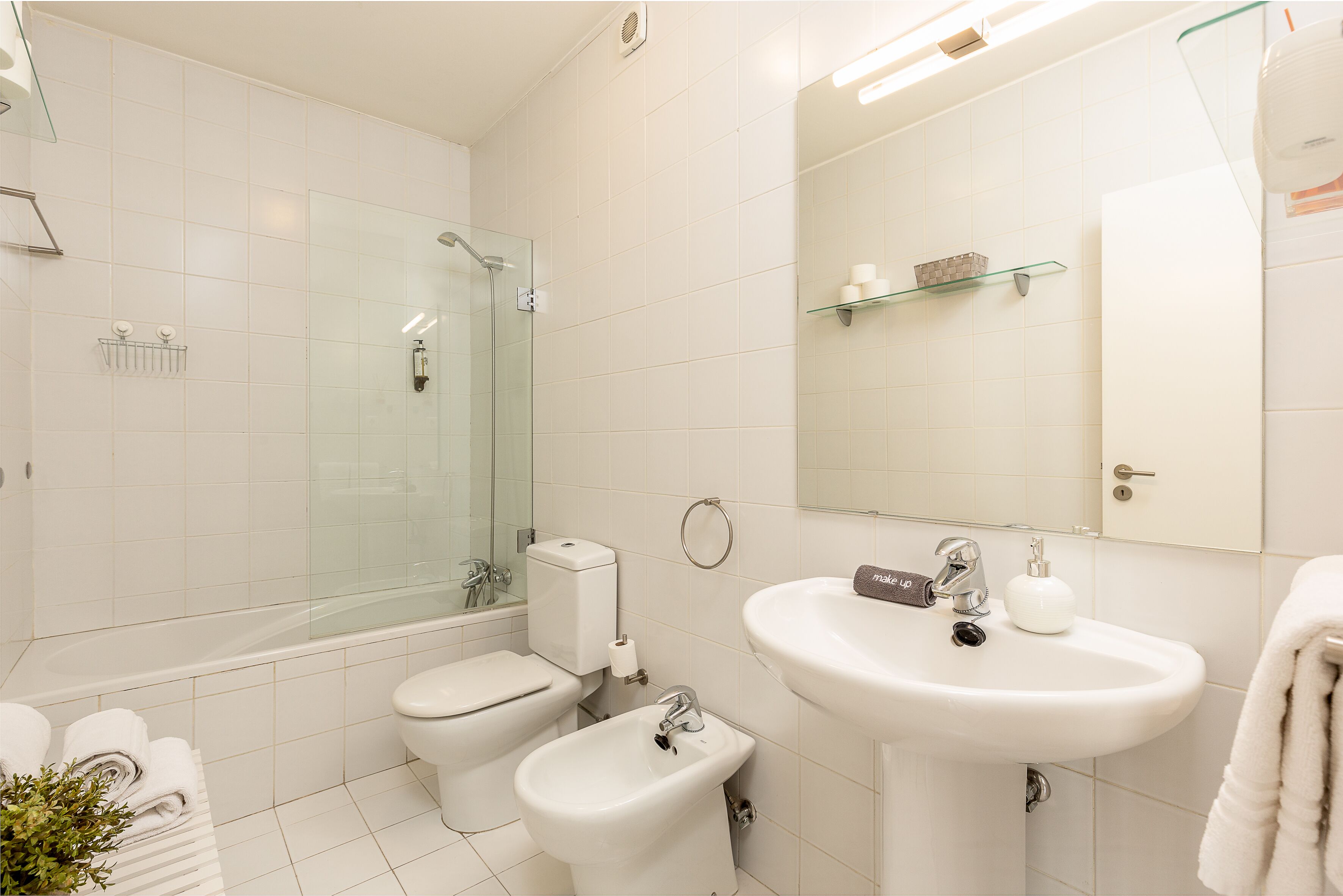 A modern bathroom with a glass-enclosed shower, a toilet, a bidet, and a sink with a mirror above.