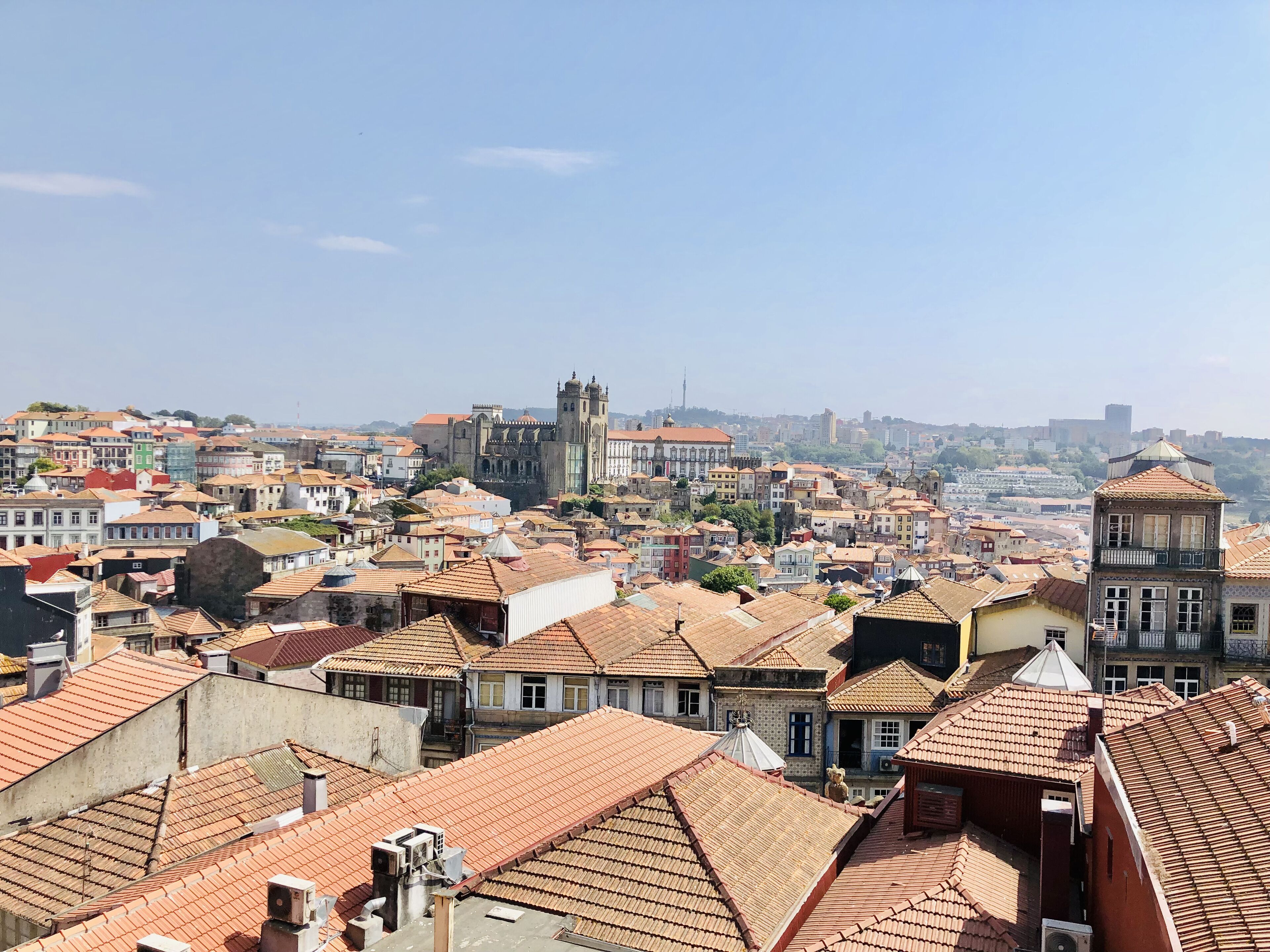A cityscape with a prominent historical building in the center, surrounded by densely packed buildings with red-tiled roofs.