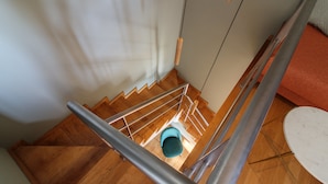 A staircase with wooden steps and metal railings, leading to a room with a white wall and a red sofa. - YOUROPO - Clérigos (Porto)