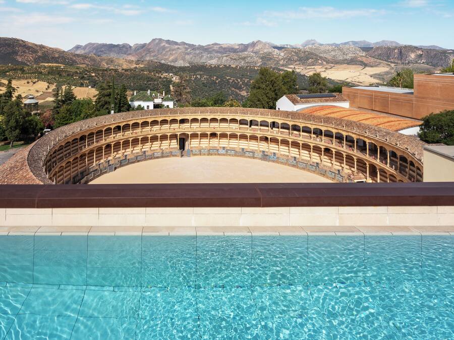 Una piscina con vistas a un anfiteatro histórico y montañas al fondo.