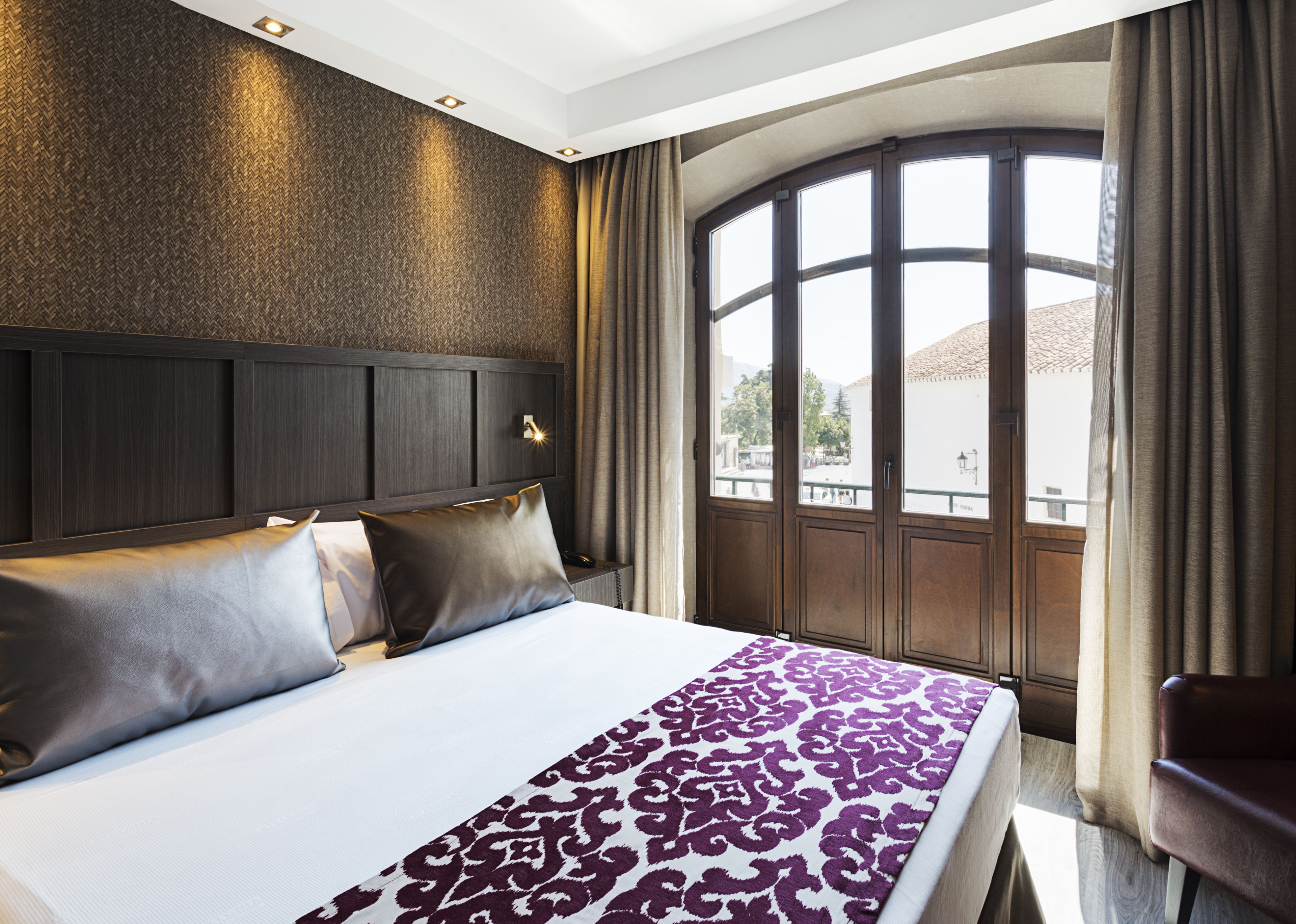 A hotel room with a large bed, a headboard, a window with curtains, and a view of the outside.