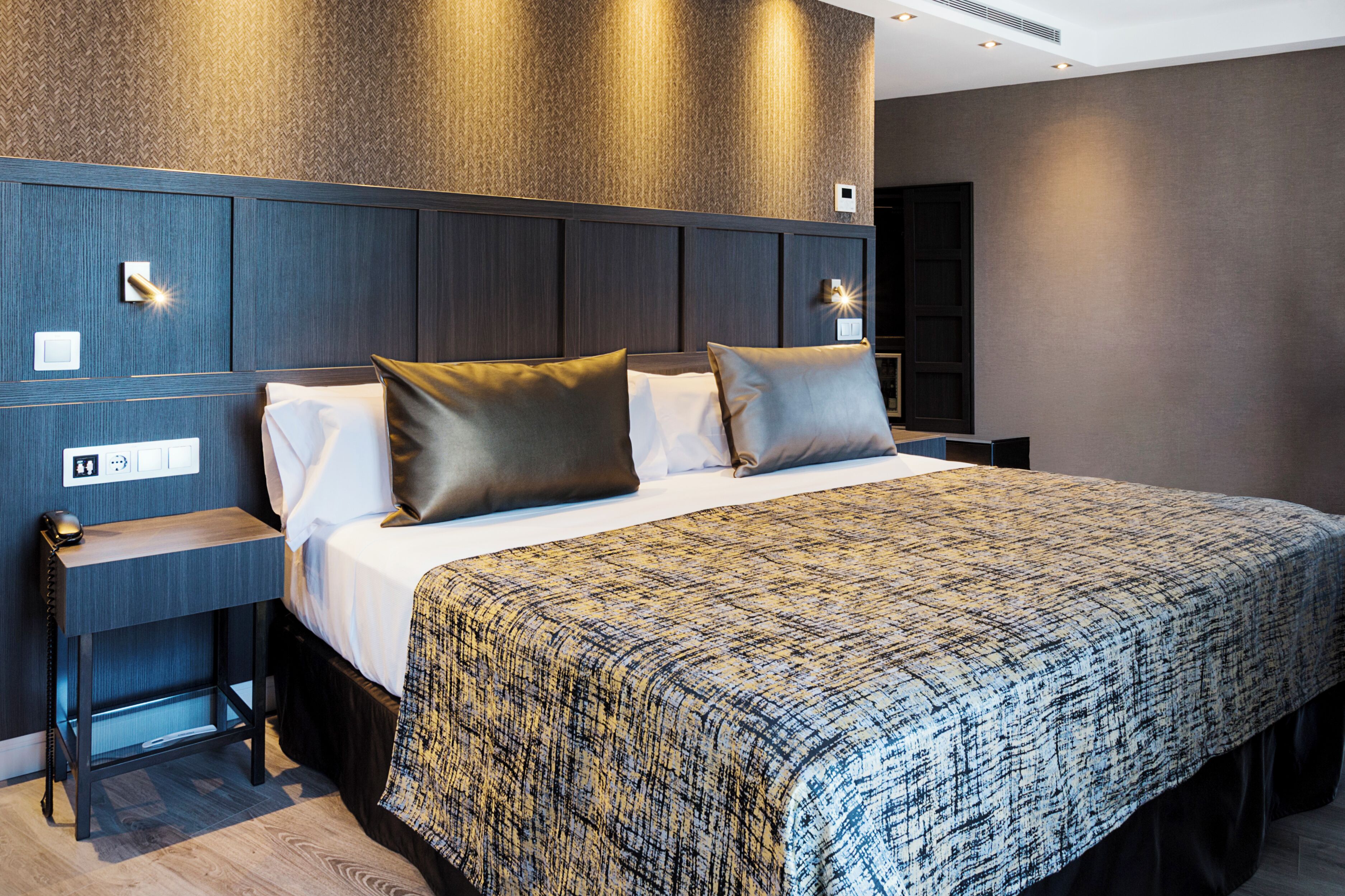 Una habitación de hotel moderna con una cama grande, una mesita de noche y una pequeña mesa auxiliar.