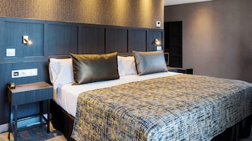 Quarto de hotel moderno com uma cama grande, uma mesinha de cabeceira e um criado-mudo.