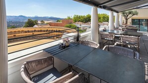 An outdoor terrace with a view of mountains, featuring wicker furniture and a large table.