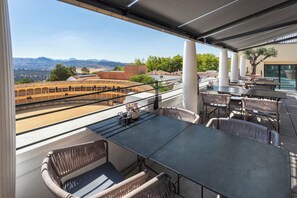 An outdoor terrace with a view of mountains, featuring wicker furniture and a large table.