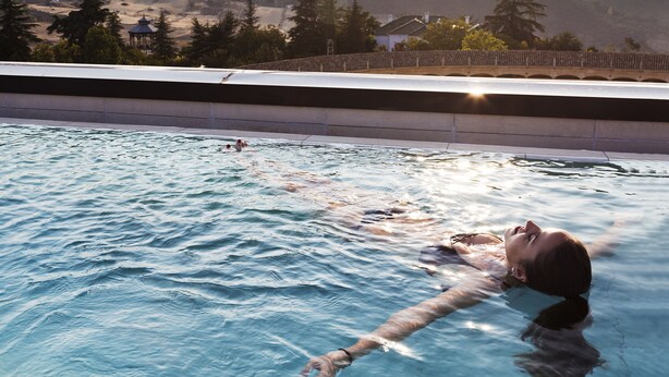 A swimming pool with a person swimming, surrounded by mountains and trees.