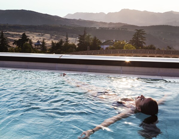 A swimming pool with a person swimming, surrounded by mountains and trees.