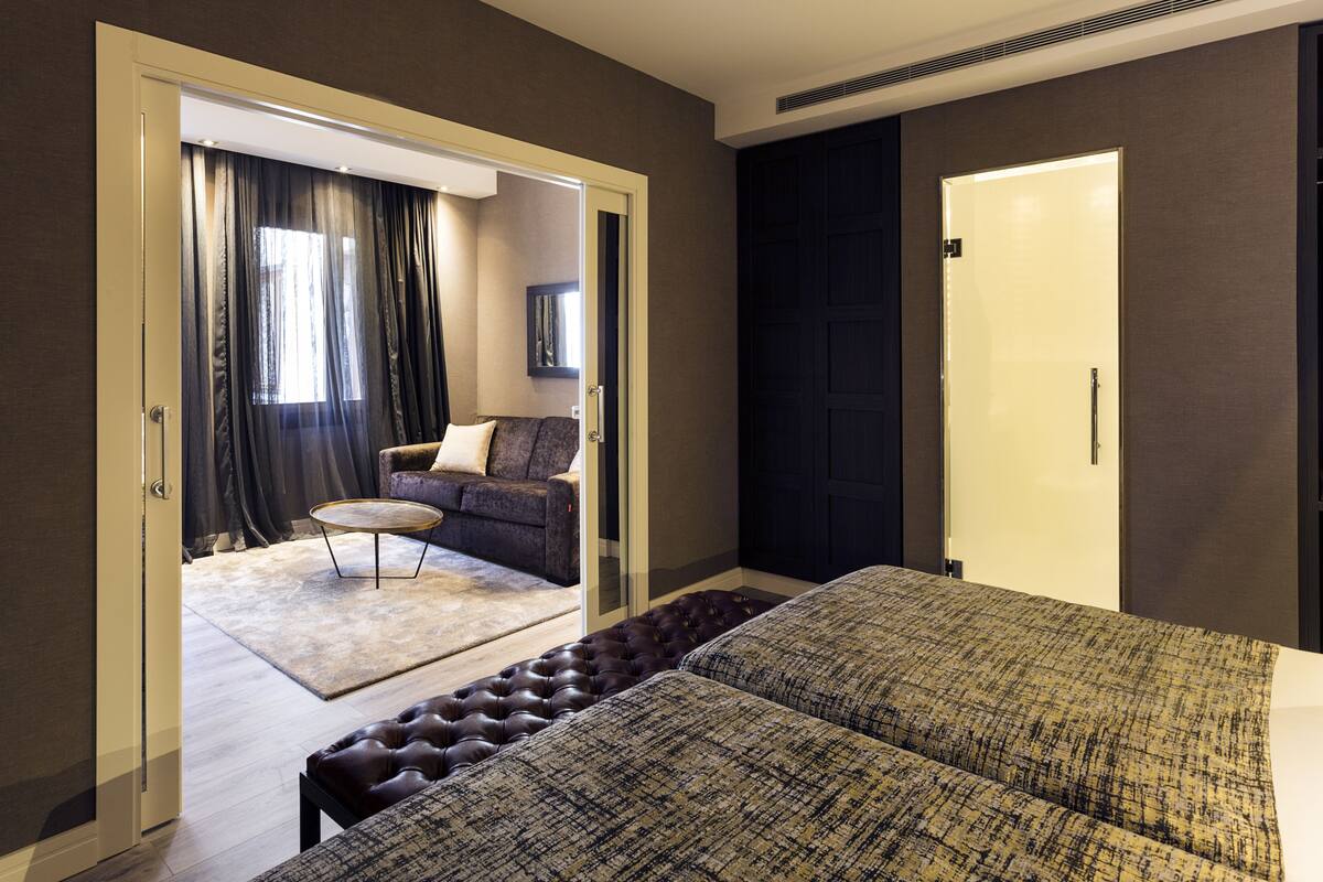 A hotel room with a large bed, a sofa, a small round table, and a door leading to another room.