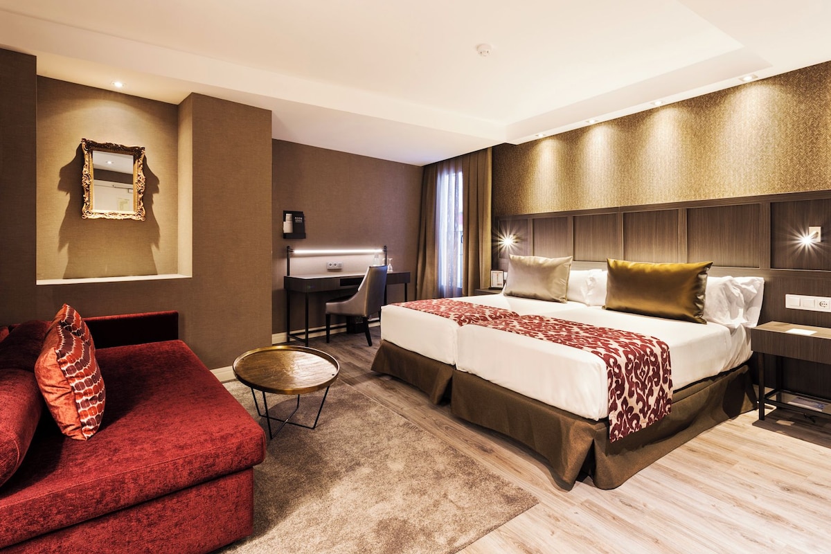 Una habitación de hotel con una cama grande, un escritorio, una silla y un sofá rojo.