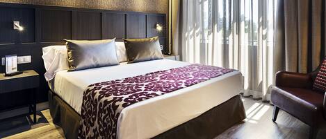 A hotel room with a large bed, a nightstand, a chair, and a view of the outdoors through the window.