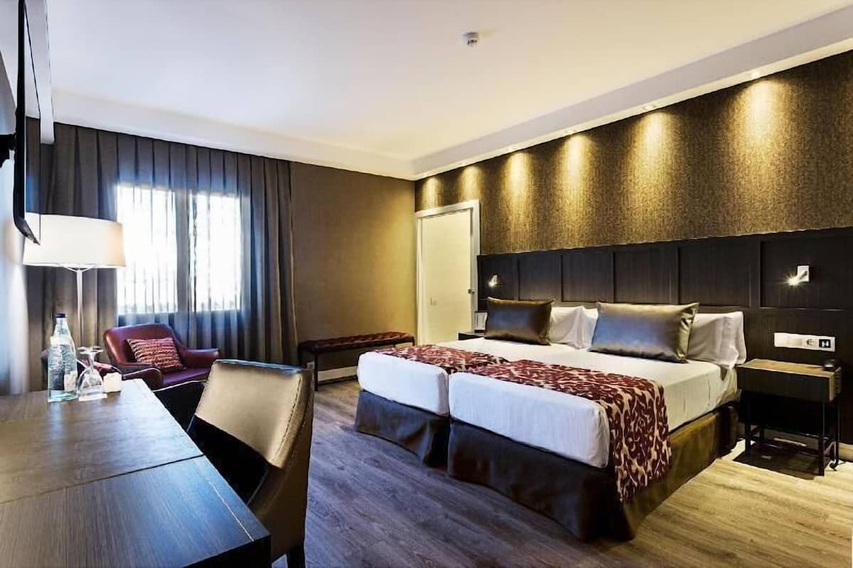 A hotel room with a bed, a desk, a chair, a lamp, and a window with curtains.