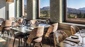A dining area with tables set for a meal, chairs with floral upholstery, and large windows offering a view of the mountains. - Catalonia Ronda (Ronda)