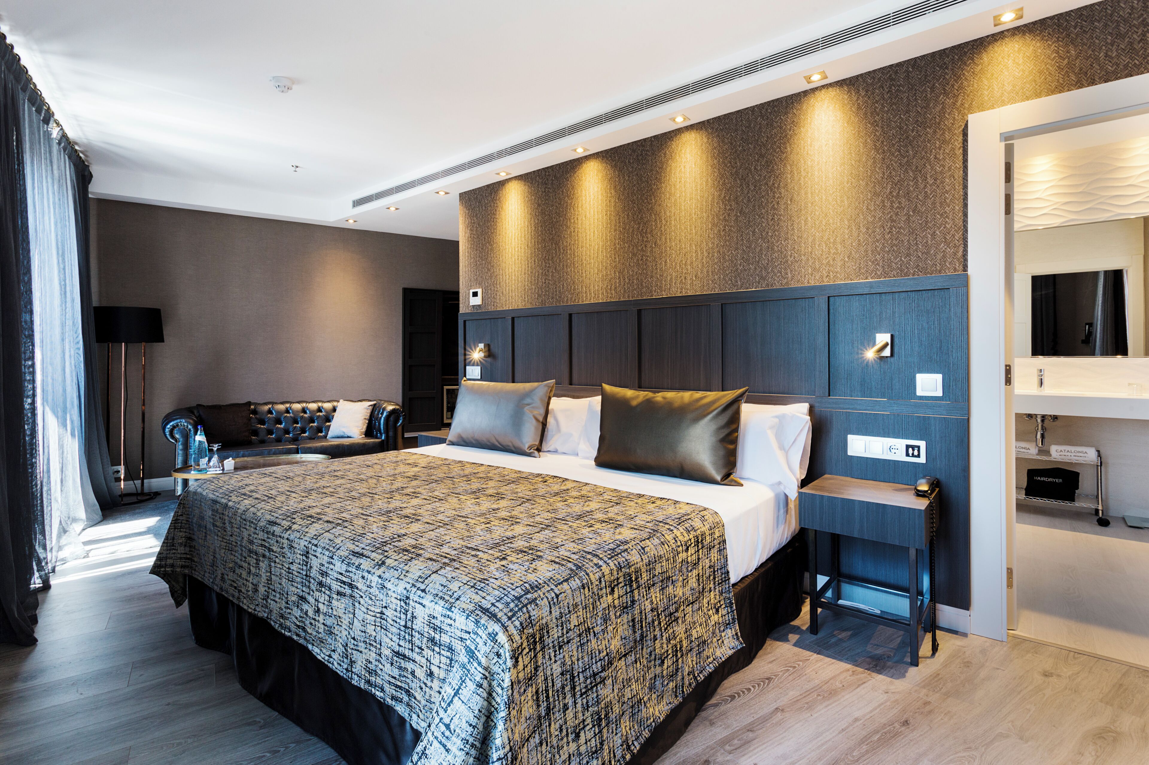 A modern hotel room with a large bed, a seating area with a sofa, and a small table.