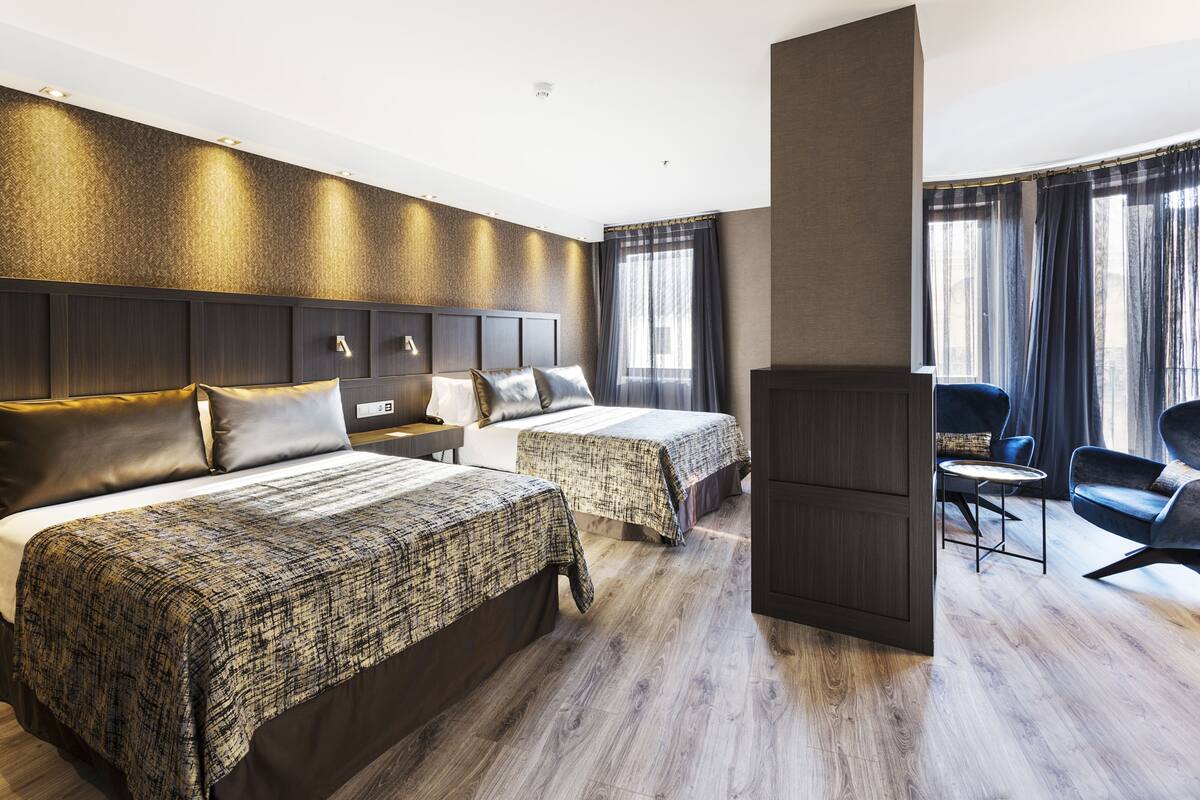 A hotel room with two beds, a desk, a chair, and a TV.