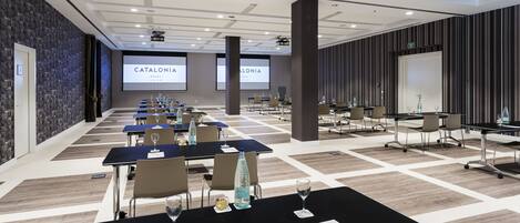 A conference room with multiple tables, chairs, and presentation screens displaying 'CATALONIA'.