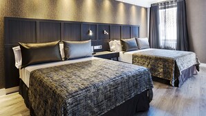 A hotel room with two beds, a dark headboard, a nightstand, and a window with curtains.