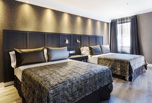 A hotel room with two beds, a dark headboard, a nightstand, and a window with curtains.
