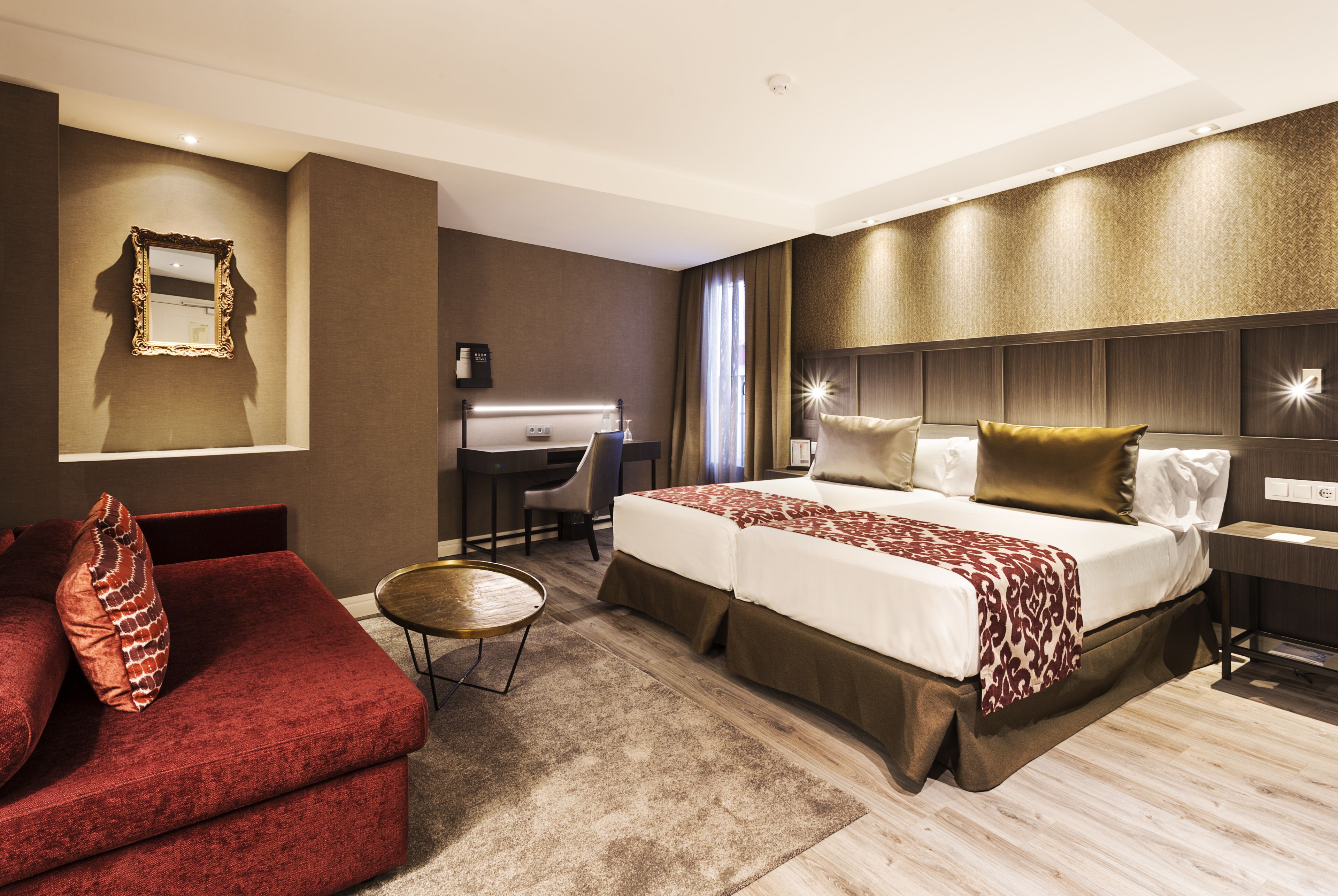 A hotel room with a large bed, a desk, a red sofa, and a mirror on the wall.