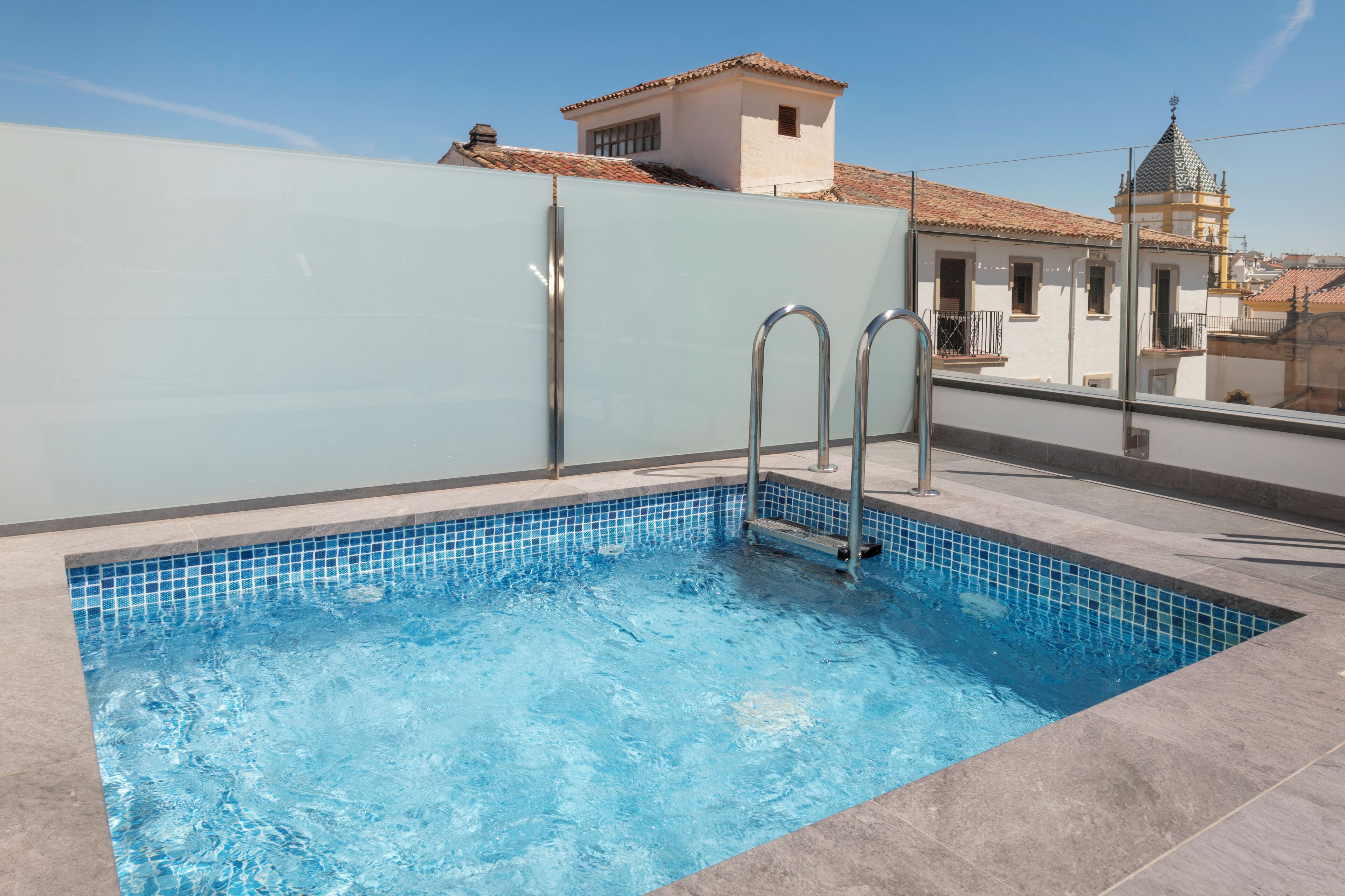 A rooftop swimming pool with clear blue water, metal ladders, and a tiled edge.