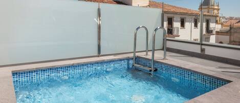 A rooftop swimming pool with clear blue water, metal ladders, and a tiled edge.