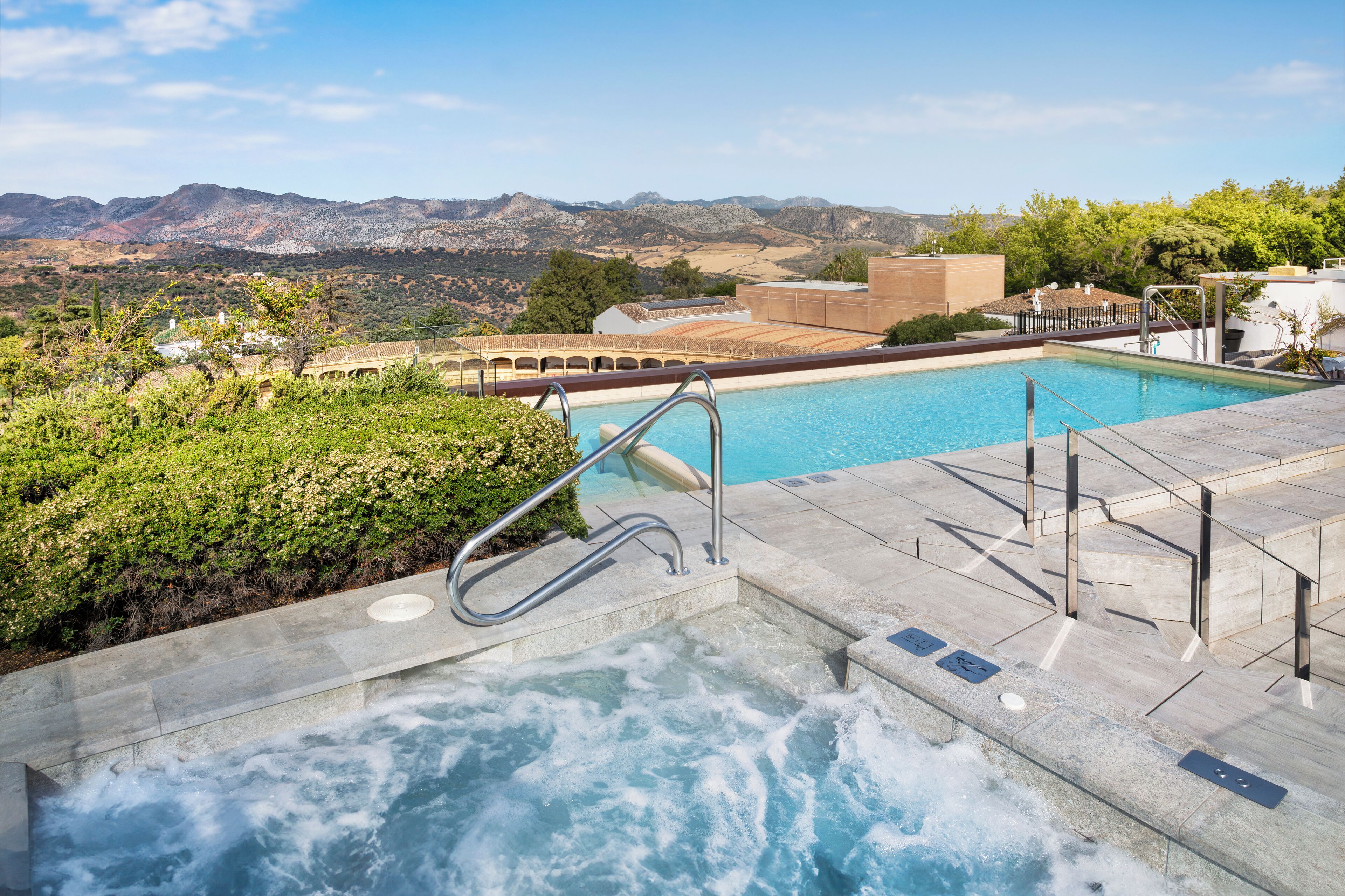 A hot tub with a view of mountains and a pool area.