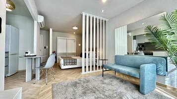 Un salon moderne avec un canapé bleu, un tapis gris et une cloison blanche.