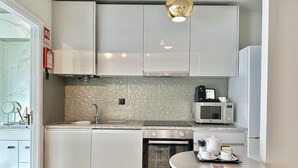 A modern kitchen with white cabinets, a granite countertop, a built-in microwave, and a small dining area with a table and chairs. - YOUROPO - Capela (Porto)