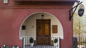 A building entrance with a wooden door, an arched overhang, and a signboard. - Leyendas del Pirineo (Fiscal)