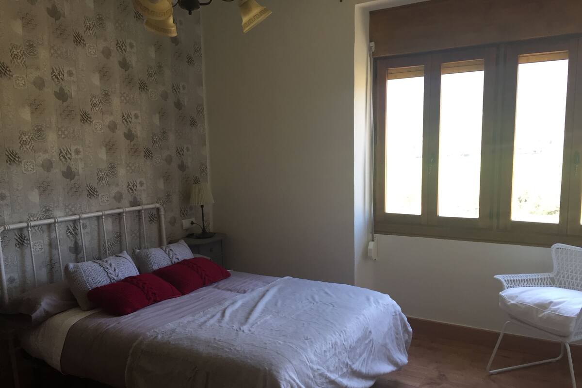 A bedroom with a bed, a nightstand, a lamp, a window, and a chair.
