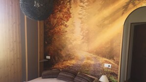 A bedroom with a large bed, a nightstand with a lamp, and a wall mural of a forest scene. - Leyendas del Pirineo (Fiscal)