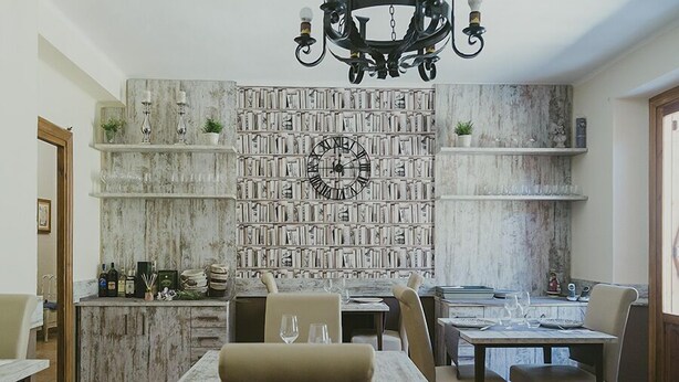 A dining area with a marble wall, bookshelves, and a chandelier. - Leyendas del Pirineo (Fiscal)