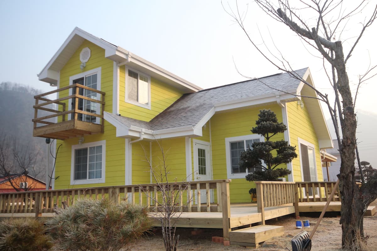 A two-story yellow house with a wooden deck and a small balcony.