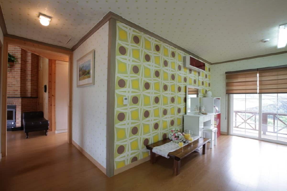 A spacious living room with a wooden floor, a patterned wall, and a large window with blinds.