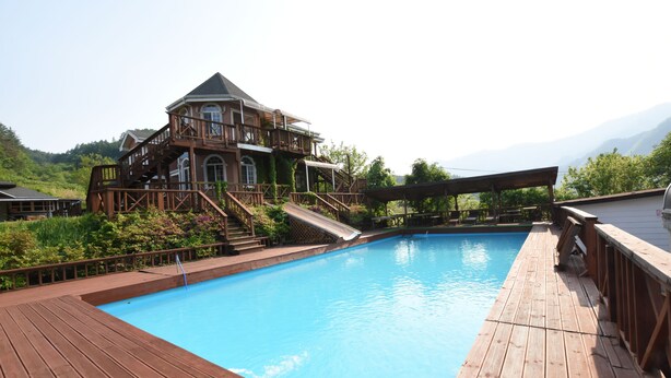 A wooden deck surrounding a swimming pool with a house in the background. - Ecopia Pension (Pyeongchang)