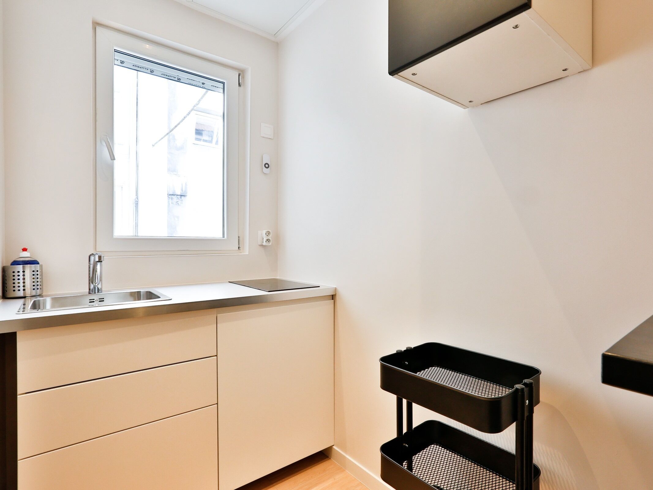A compact kitchen with a window, a sink, and a black metal rack.