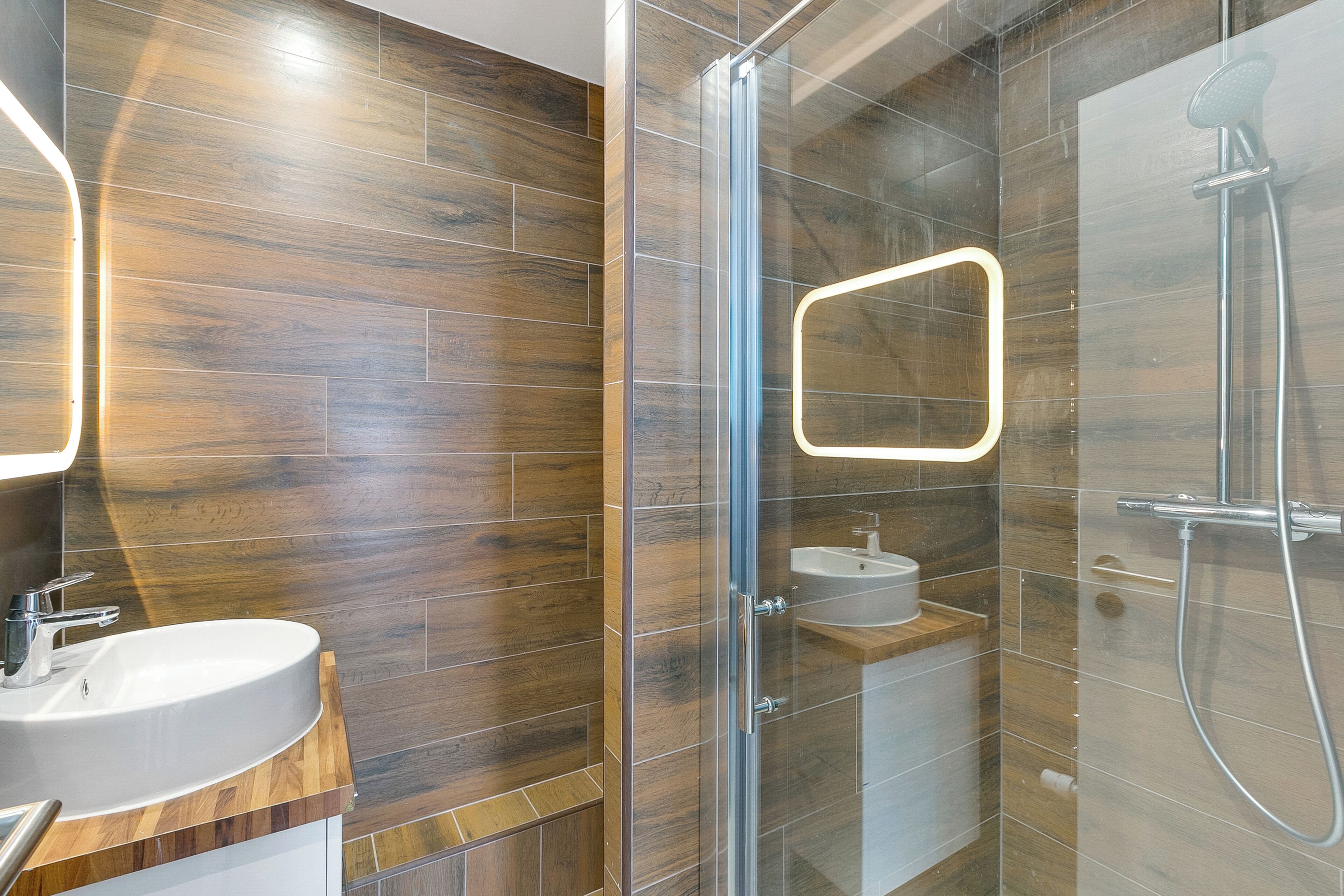 Une salle de bain moderne avec un plancher en bois, une douche à parois de verre et un lavabo avec un miroir.