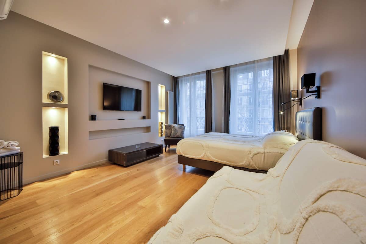 A modern bedroom with a large bed, a TV mounted on the wall, and a seating area with a chair and a small table.