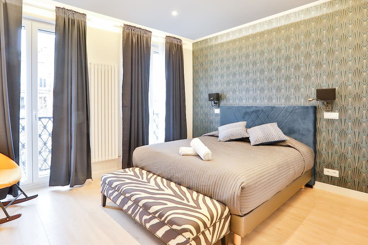 A bedroom with a large bed, a zebra-patterned bench, and a view of the outside through a sliding door.
