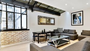 Een moderne woonkamer met een bakstenen muur, een glazen salontafel, een bank en een eettafel met stoelen.