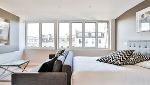 Een moderne slaapkamer met een groot raam, een bed, een bank en een kleine tafel.