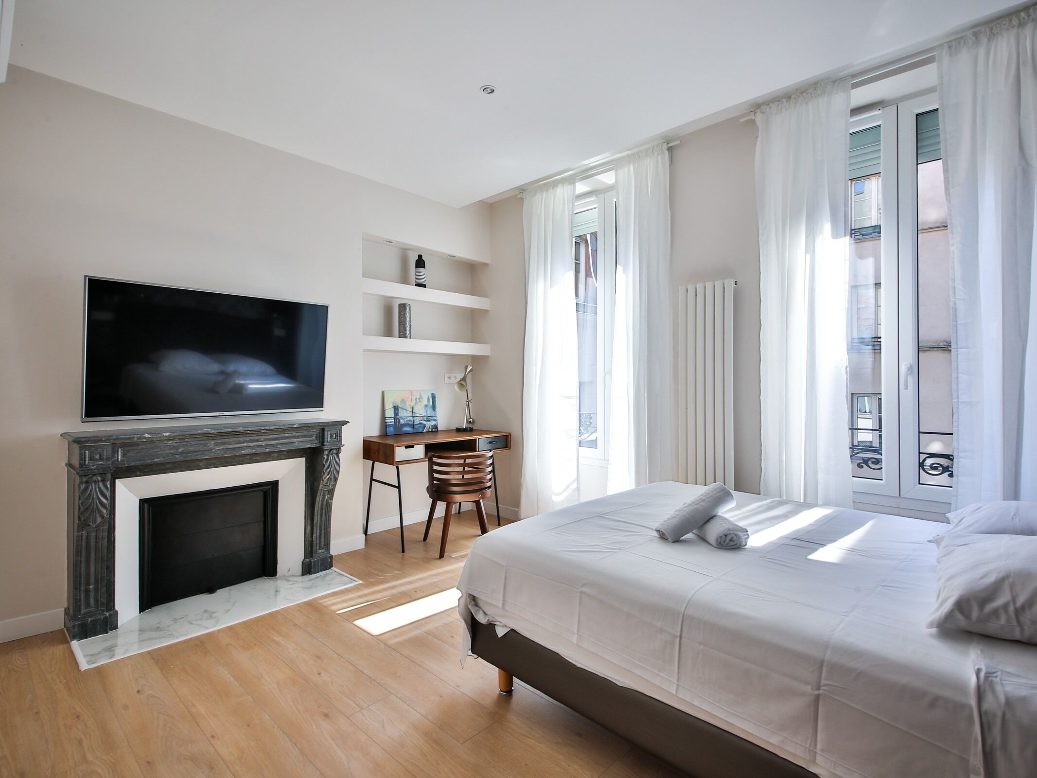 A modern bedroom with a fireplace, a TV, a desk with a chair, and a large bed.