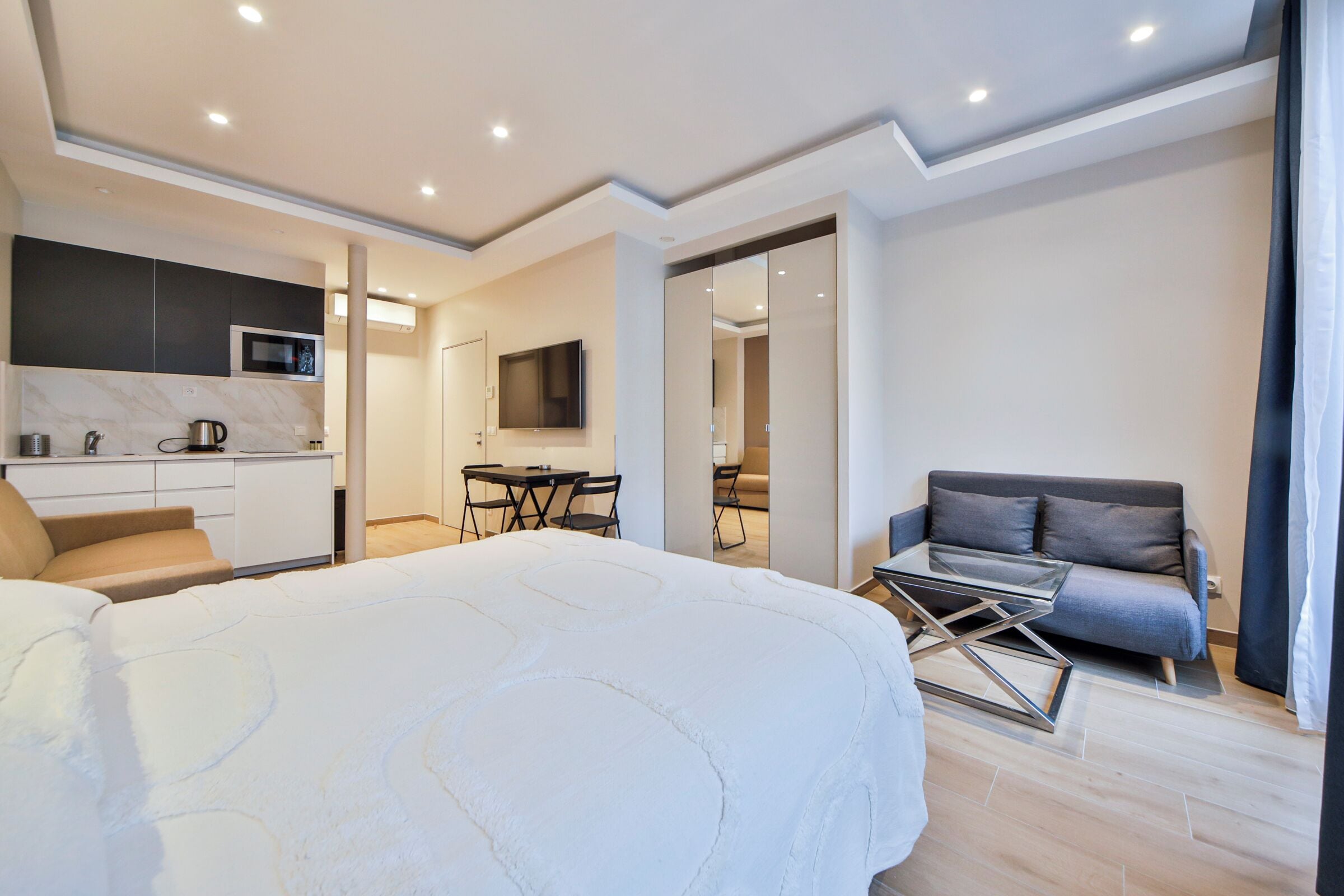 Un dormitorio moderno con una cama grande, un sofá, una mesa de comedor y una zona de cocina.