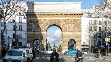 A street scene with a large stone archway, vehicles, and buildings.